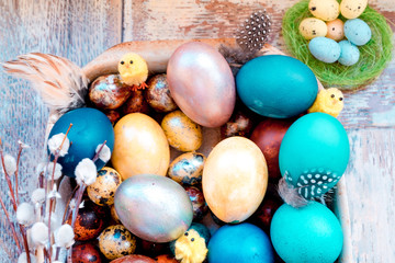 On the old wooden shabby table a dish of metal with painted in different colors Easter eggs with feathers willow and chickens