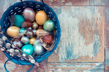 On the old wooden shabby table a dish with painted in different colors Easter eggs with feathers willow