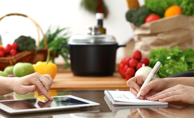 Close-up of human hands using tablet or touch pad. Two women in kitchen. Cooking, friendship or family fun concepts