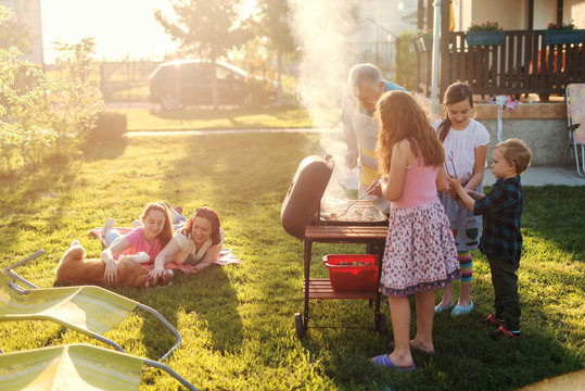 Grandfather teaching his grandchildren how to grill meal. Family gathering in backyard concept.