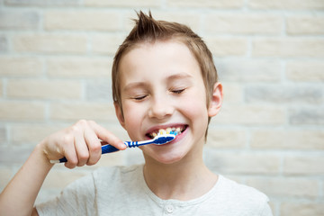 Cute boy shows his teeth and toothbrush. Light background
