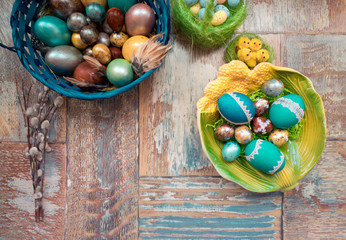 On the old wooden shabby table a dish with painted in different colors Easter eggs with feathers willow and chickens with rabbit