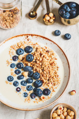 Top view on healthy breakfast, a bowl with organic granola, chocolate pieces, fresh blueberries, hazelnuts and soya milk.