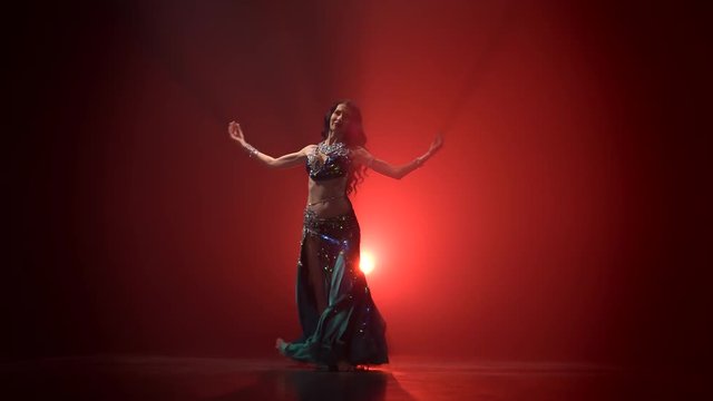 Traditional oriental belly dancer girl dancing . Red smoke background