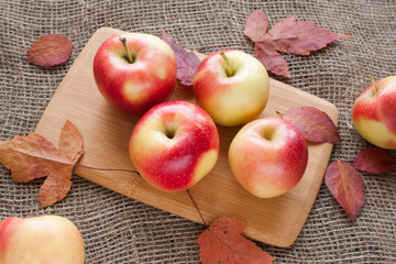 apples on a cutting Board on a burlap with dry autumn leaves