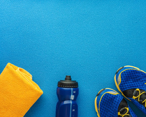 Sports equipment flat lay composition, running shoes, yellow towel and bottle of water on blue background. Concept healthy lifestyle, sport and diet.