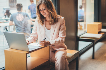 Happy successful business woman working at laptop while sitting in coffee shop, smiling female entrepreneur using computer for work or studying in cafe, concept of distant work and online education