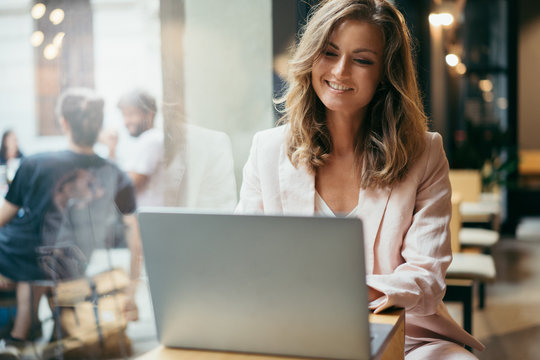 Happy successful business woman having a video call via laptop while sitting in coffee shop, smiling female entrepreneur having a distant meeting or online lesson at computer sitting at cafe