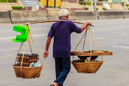 Street hawker is walking with carry bamboo baskets of grilled eggs on shoulder pole go around Bangkok, Thailand.
