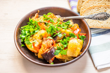 Roast vegetables on a rustic plate, standing on a light wooden table - a healthy organic dish.