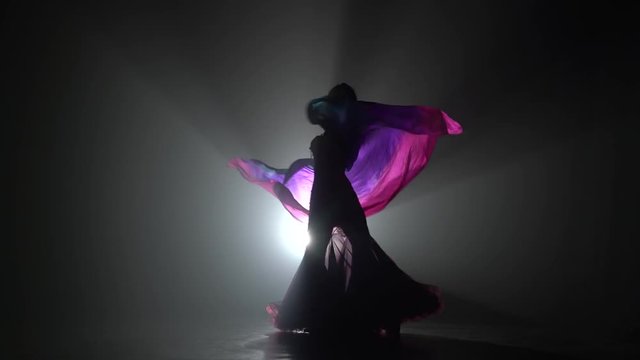 Girl dancing belly dance with shawl. Sihouette . Black smoke background