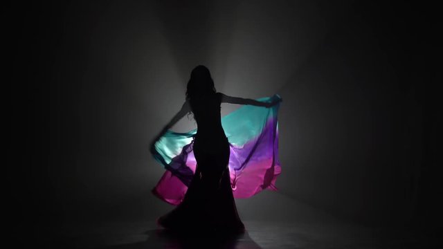 Girl starts dancing belly dance with shawl. Sihouette . Black smoke background