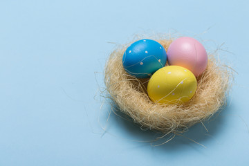 Colorfull easter eggs in nest on blue pastel color background with space.