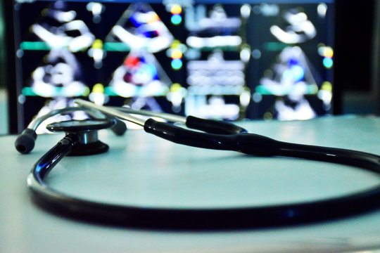 Focus A Stethoscope On White Table, Blurred Background Is Screen Of Echocardiogram (ultrasound Of Haert). Dark Tone Is Applied.