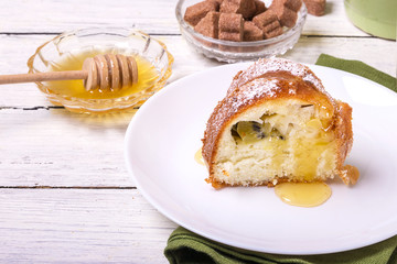 A piece of sweet round fruit homemade cake, on a white dish on a wooden table, served with a cup of milk