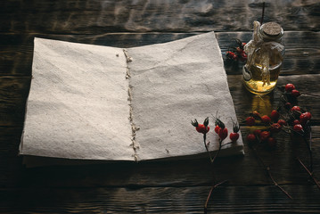 Briar berry essential oil and blank page open book with recipe on a wooden table. Herbal medicine top view background with copy space.