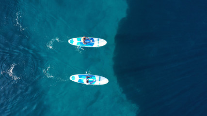 Aerial drone bird's eye view of 2 men exercising sup board in turquoise tropical clear waters