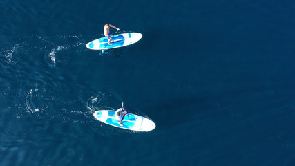 Aerial drone bird's eye view of 2 men exercising sup board in turquoise tropical clear waters