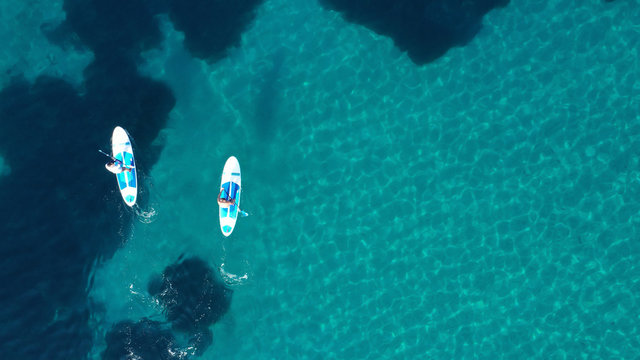 Aerial drone bird's eye view of 2 men exercising sup board in turquoise tropical clear waters
