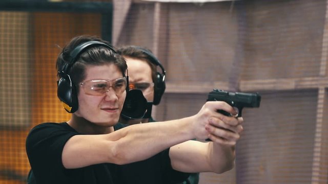 Shooting gallery. A concentrated young man in protective glasses and headphones aiming in a target and shoot