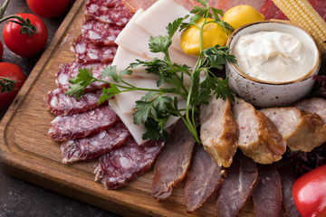 Tasty appetizer with sliced from different types of sausages and smoked meats with horseradish sauce and pickles . Closeup