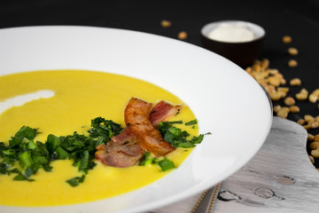 Pea soup with pieces of bacon, parsley and onion in a bowl on a dark background. Pea cream soup. Macro