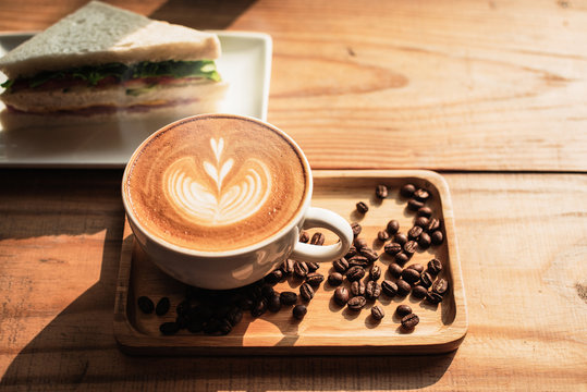 A cup of coffee with heart pattern in a white cup and Sandwich on wooden table background - Image