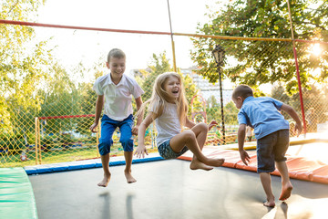 Group of children jump on trampoline in the park - obrazy, fototapety, plakaty