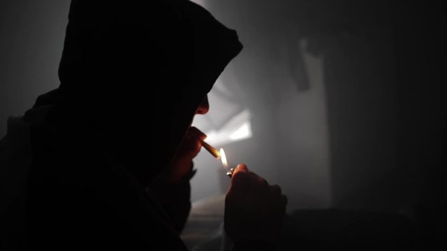 A young man lights up a marijuana joint and smokes it.