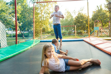 Two boys and girl jump on trampoline outdoor in summer day