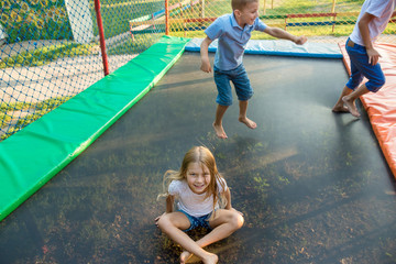Two boys and girl jump on trampoline outdoor in summer day