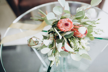 on the glass table is a box with wedding rings, next to it is a bouquet of flowers and greenery