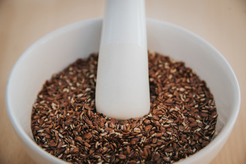 Leinsamen geschrotet in einer weißen Schüssel mit Mörser auf Holz Hintergrund