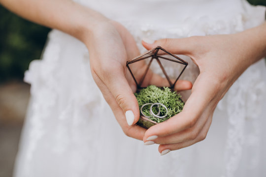 girl in a white dress is holding a glass box in which are wedding rings