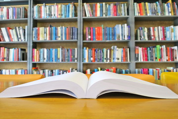 The old book open on the wooden table in the library. Selective focus with blurred bookshelves background. Education and book's day concept.