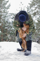 Fototapeta premium Warmly dressed man embracing loveful young russian spaniel dog in the winter forest