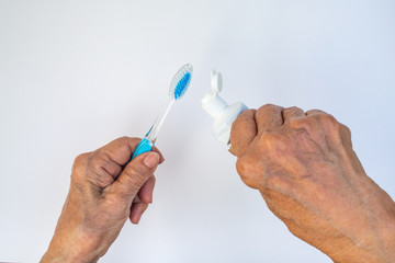 Senior woman's hands squeezing toothpaste on brush against isolated on white background