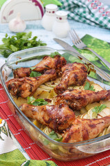 Baked chicken drumstick with potatoes and zucchini in glass form. The photo has a fork, knife and jars of salt and pepper