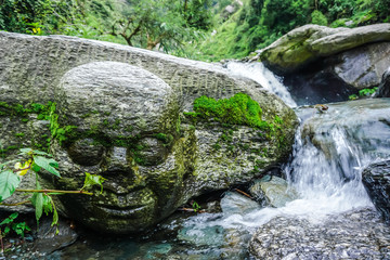 Naklejka na ściany i meble A human head carved in one of the stones of a mountain river in the wild. Dharamsala, India