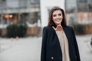 A young beautiful woman with long,hair and gray eyes,beautiful makeup,pink plump lips,sweet smile,brunette,spending her time outdoors in the spring in the city.Portrait of happy young woman in a cap