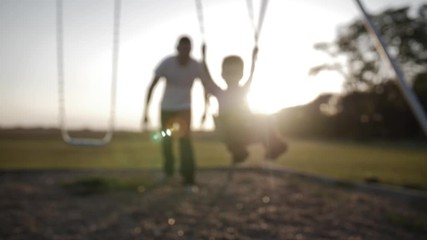 A father pushes his son on a swingset