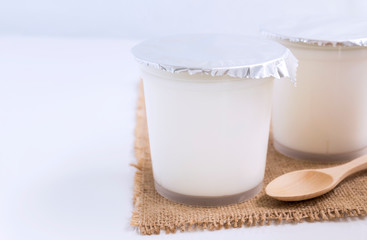 Healthy flavored yogurt in plastic cup with wooden spoon on the sackcloth with isolated on white background. with copy space for text.