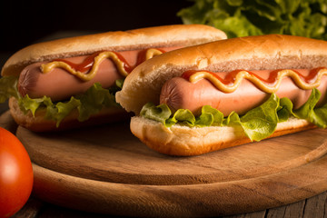 Photo of barbecue grilled hot dog with yellow mustard and ketchup on wooden background. Hot dog sandwich with potato fries and sauces.