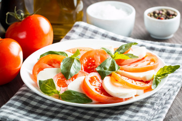 Photo of Caprese Salad with tomatoes, basil, mozzarella, olives and olive oil on wooden background. Italian traditional caprese salad ingredients. Mediterranean, organic and natural food concept.