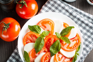 Photo of Caprese Salad with tomatoes, basil, mozzarella, olives and olive oil on wooden background. Italian traditional caprese salad ingredients. Mediterranean, organic and natural food concept.