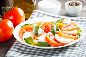 Photo of Caprese Salad with tomatoes, basil, mozzarella, olives and olive oil on wooden background. Italian traditional caprese salad ingredients. Mediterranean, organic and natural food concept.