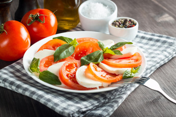 Photo of Caprese Salad with tomatoes, basil, mozzarella, olives and olive oil on wooden background. Italian traditional caprese salad ingredients. Mediterranean, organic and natural food concept.