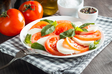 Photo of Caprese Salad with tomatoes, basil, mozzarella, olives and olive oil on wooden background. Italian traditional caprese salad ingredients. Mediterranean, organic and natural food concept.