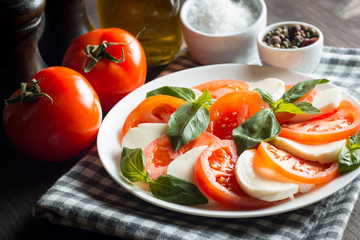 Photo of Caprese Salad with tomatoes, basil, mozzarella, olives and olive oil on wooden background. Italian traditional caprese salad ingredients. Mediterranean, organic and natural food concept.