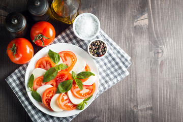 Photo of Caprese Salad with tomatoes, basil, mozzarella, olives and olive oil on wooden background. Italian traditional caprese salad ingredients. Mediterranean, organic and natural food concept.